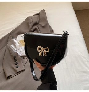 Detail of black glossy leather saddle bag featuring a gold butterfly buckle and adjustable strap