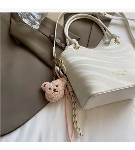 Detail of creamy white wave-patterned bucket bag with cute bear charm and golden hardware
