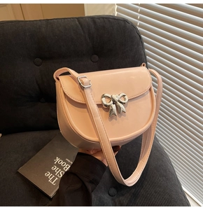 Detail of a pink leather saddle bag featuring a silver metal heart bow buckle detail