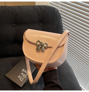 Detailed view of pink saddle bag with silver bow hardware on textured black background