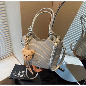 Detail of silver wavy texture handbag with brand logo and brown plush bear charm