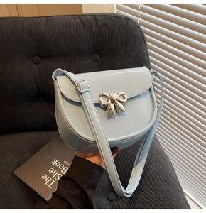 Detail of light blue saddle bag with silver metal bow clasp on gray fabric sofa