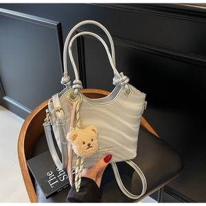 Detailed view of silver shoulder bucket bag with wavy texture and bear charm