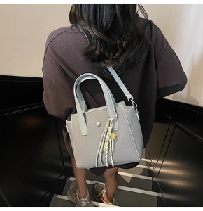 Détail du sac seau bleu clair tissé avec foulard en soie et breloque pompon jaune