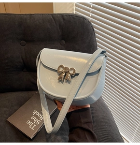 Detail of light blue saddle bag featuring a silver bow buckle and glossy leather finish