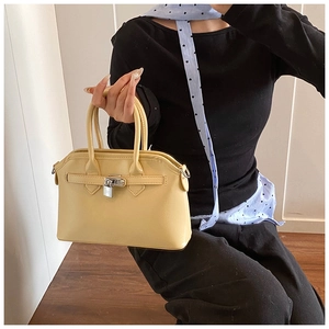 Close-up of yellow leather handbag featuring silver metal twist lock and dual top handles