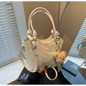 Detail of cream-colored bucket bag with wave texture and bear charm in a mirror setting