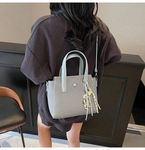 Détail d'un sac seau gris avec texture tressée et breloque ours porté par un mannequin