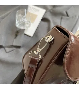 Gros plan sur la texture en cuir verni marron foncé et le crochet en métal argenté