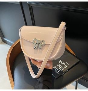 Detail of light pink saddle bag featuring a silver metal bow clasp and adjustable strap