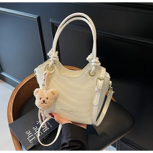 Detail of white wavy texture handbag with gold rings and brown plush bear charm