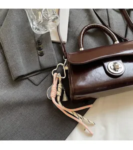 Détail d'un sac à main en cuir marron foncé avec fermoir métallique et pendentif de tennis