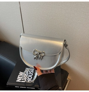 Detailed view of silver saddle bag with metallic bow buckle against a beige wall
