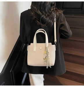Sac seau tissé beige avec breloque ours et pompon porté par un mannequin