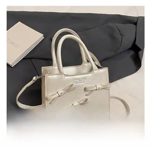 Detailed close-up of cream bow handbag with metallic logo and textured pearl finish