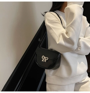 Detail of black faux leather crossbody bag featuring a silver metal bow buckle