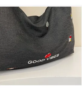 Dettaglio borsa tote in denim scuro con motivi ricamati colorati e scritta Good Vibes