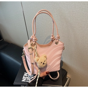 Pink shoulder bag detail showing wave texture, cylindrical handles, and a cute teddy charm