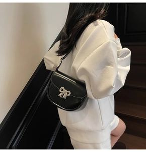 Detailed view of black saddle bag with silver metal bow on a model's shoulder