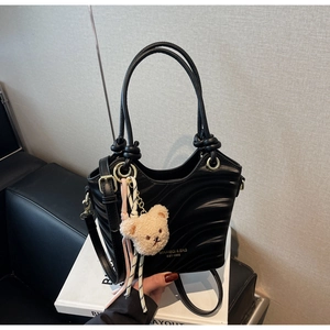Detail of black wave textured bucket bag with plush bear charm and gold metal hardware