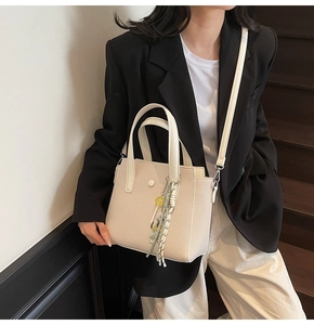 Détail d'un sac seau beige avec texture tissée et foulard en soie sur un mannequin