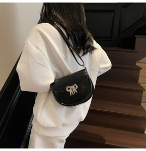 Detail of black glossy saddle bag with a silver metal bow buckle on a white sweatshirt