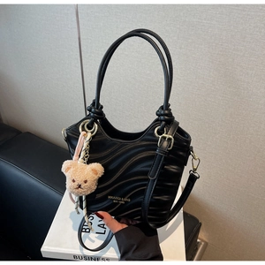 Close-up of black wave-textured handbag featuring a gold logo and a cute plush bear charm