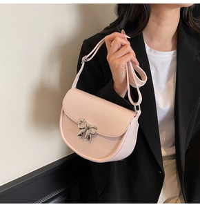 Detail of light pink saddle bag with silver bow accent on a black blazer outfit