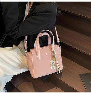 Sac seau rose tissé avec pendentif ours porté en bandoulière sur un mannequin élégant