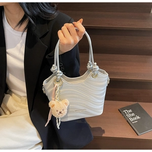 Detail of silver gray handbag with wavy texture, plush bear charm and silk scarf decoration