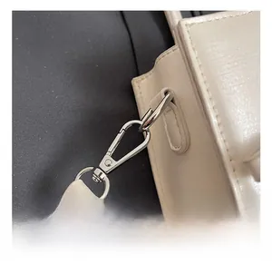Detailed macro view of silver metal hook and leather texture on cream crossbody bag