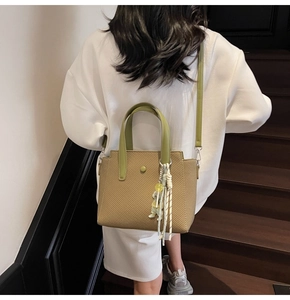 Détail du sac seau tissé kaki avec anses vertes porté par un mannequin dans un escalier