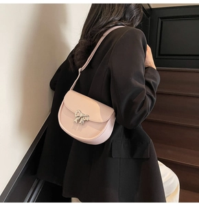 Detail of light pink saddle bag with silver bow buckle worn over black blazer