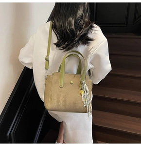 Détail du sac seau tissé avec lanières en cuir vert et accessoire à pampilles rayées