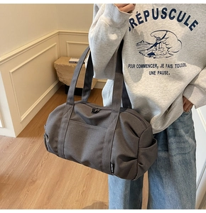 On-body view of dark grey canvas travel duffel bag with handles and brand tag
