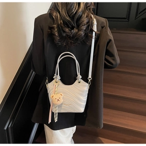 Detail of silver shoulder bag with ripple texture and plush bear charm on wooden stairs