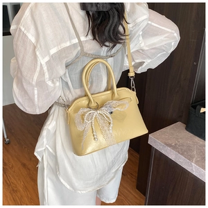 Detail shot of a cream yellow crossbody bag with delicate lace and pearl bow accents