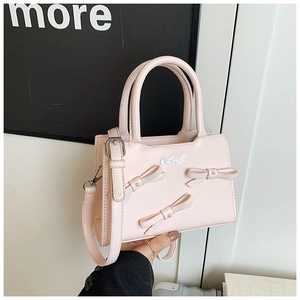 Detail of pink leather handbag with decorative pearl-centered bows and adjustable strap