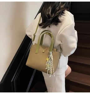 Détail d'un sac seau tissé marron clair avec poignées en cuir vert et pendentif poupée