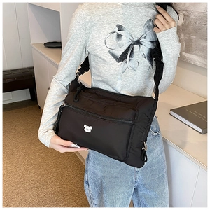 Detail of black nylon crossbody bag featuring cute white bear patch and ruffled shoulder strap