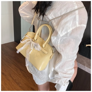 Detail of light yellow leather handbag with lace trim and pearl bow decoration
