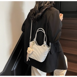 Close-up of silver wavy bucket bag with plush bear charm and metallic logo detail
