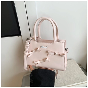 Close-up of pink crossbody bag with decorative bows and pearls held by hand