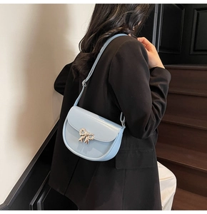 Close-up of light blue saddle bag featuring a gold bow buckle on black suit model