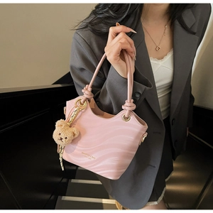 Detail of pink wave-textured bucket bag with a knotted handle and plush bear charm
