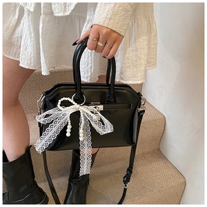Detail of glossy black handbag featuring white lace bow and elegant pearl charm detail