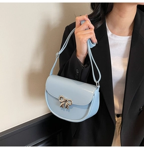 Close-up of light blue saddle bag with silver bow buckle on model in black blazer