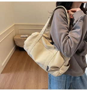 Close-up of beige canvas travel bag featuring wide shoulder straps and brand woven label
