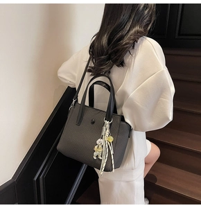 Détail du sac seau noir tressé avec breloque ours et bandoulière réglable chic