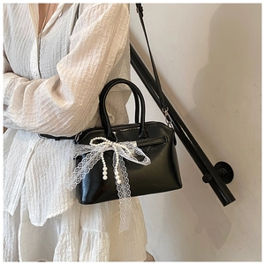 Fashionable black leather handbag with pearl lace bow detail worn by a model in casual style